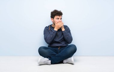 Genç adam yerde oturup ağız kapsayan ve yan bakıyor