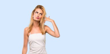 İzole edilmiş mavi arka planda intihar jesti yapan genç sarışın kadın.