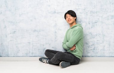 Asyalı adam kollarını çapraz ve mutlu ile katta oturan