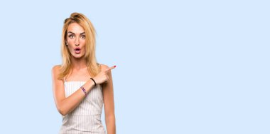 Genç sarışın kadın şaşırmış ve mavi arka planı işaret ediyor.