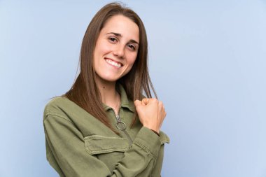 İzole mavi duvar üzerinde genç kadın bir zafer kutluyor