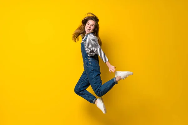 Młoda dziewczyna z kombinezonu skoki na białym tle żółty — Zdjęcie stockowe