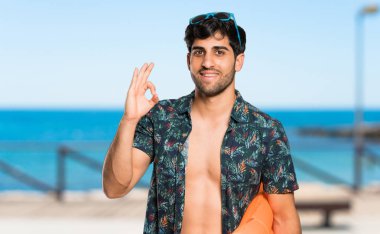 Plajda parmaklarıyla ok işareti gösteren şort adam