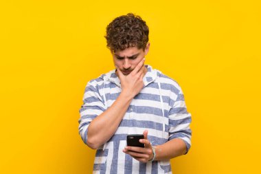 Bir mobil ve düşünme ile sarı duvar üzerinde Sarışın adam