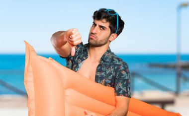 Plajda olumsuz ifade ile başparmak aşağı gösteren şort adam