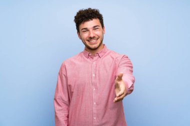 Izole mavi duvar üzerinde kıvırcık saçlı adam iyi bir anlaşma kapanış için el sıkışma