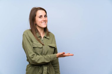 İzole mavi duvar üzerinde genç kadın gelmeye davet için yan ellerini uzatan