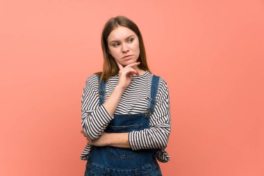 Pembe duvarın üstünde eli çenesinde genç bir kadın var.