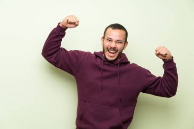 Bir zafer kutluyor yeşil duvar üzerinde Sweatshirt ile Kolombiyalı adam