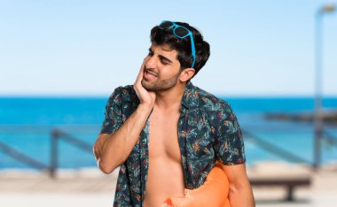 Plajda diş ağrısı olan şortlu adam
