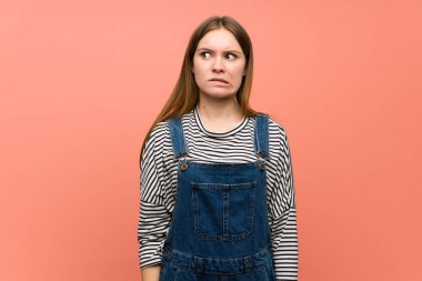 Pembe duvarda tulumlu genç bir kadın biraz gergin ve dişlerini sıkmaktan korkuyor.