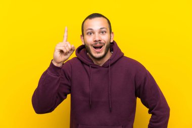 Sarı duvar üzerinde sweatshirt ile Kolombiyalı adam bir parmak kaldırırken çözüm gerçekleştirmek niyetinde