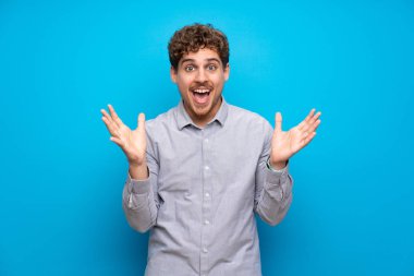 Sarışın adam şok yüz ifadesi ile mavi duvarın üzerinden