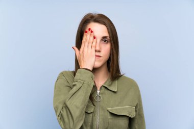 Young woman over isolated blue wall covering a eye by hand