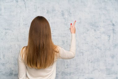 İşaret parmağıyla işaret eden grunge duvarının arkasındaki genç kadın.