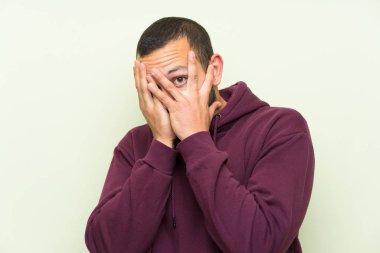 Gözleri kaplayan ve parmaklardan bakan yeşil duvar üzerinde sweatshirt ile Kolombiyalı adam