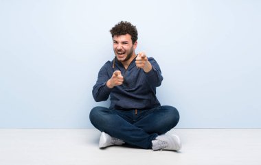 Genç adam yerde oturuyor, ön tarafı gösteriyor ve gülümsüyor.