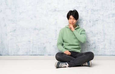 Asyalı adam ağzına parmak koyarak sessizlik jest bir işaret gösteren katta oturan