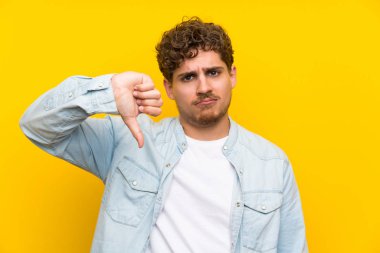Sarışın adam başparmak işareti aşağı gösteren izole sarı duvarın üzerinden