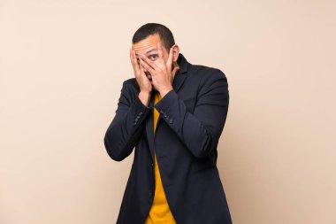 Gözleri kaplayan ve parmaklardan bakan izole arka plan üzerinde Kolombiyalı adam