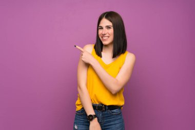 Bir ürün sunmak için yan işaret izole mor duvar üzerinde genç kadın