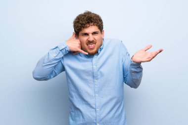 Sarışın adam telefon jest yapma ve şüphe mavi duvarın üzerinden