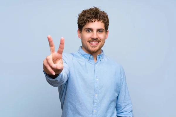 Blond Man Över Blå Vägg Leende Och Visar Tecken Seger — Stockfoto