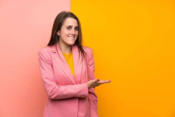 Young Woman Pink Suit Colorful Background Extending Hands Side Inviting — Zdjęcie stockowe