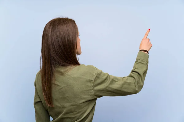 人差し指で後ろを指す孤立した青い壁の上の若い女性 — ストック写真