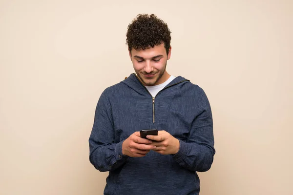 Człowiek Kręconymi Włosami Nad Izolowaną Ścianą Wysyłającą Wiadomość Telefonem — Zdjęcie stockowe