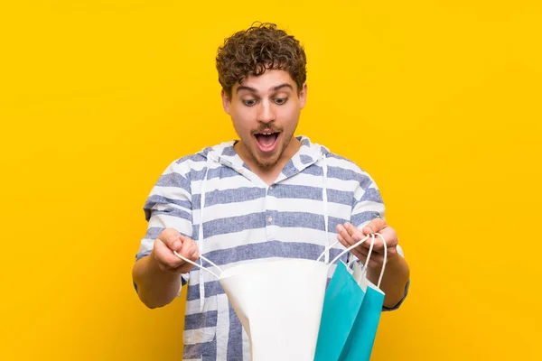 Sarı Duvar Üzerinde Sarışın Adam Alışveriş Çantaları Bir Sürü Tutarken — Stok fotoğraf
