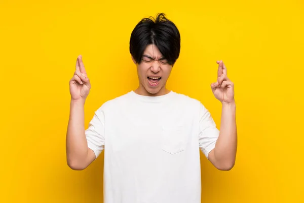 指が交差する孤立した黄色い壁の上のアジアの男性 — ストック写真