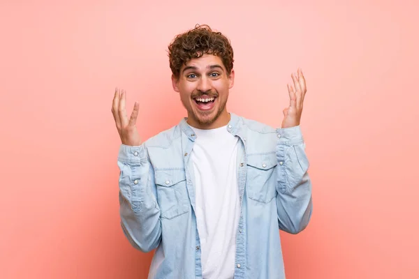 Blonde man over pink wall smiling with a sweet expression