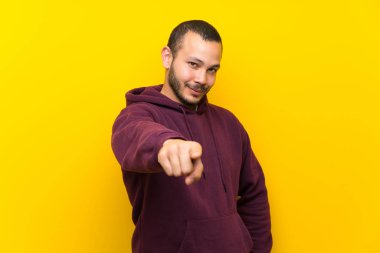 Sarı duvar noktaları üzerinde sweatshirt ile Kolombiyalı adam kendine güvenen bir ifade ile size parmak