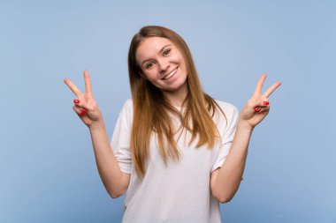 Mavi duvara gülümseyen ve her iki eliyle zafer işareti gösteren genç kadın