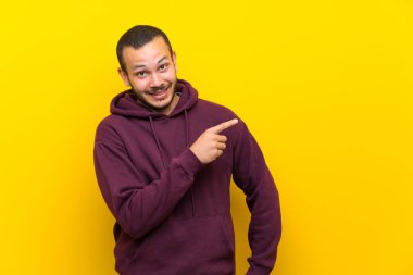 Sarı duvar üzerinde kazak ile Kolombiyalı adam yan parmak işaret