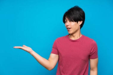 Avuç içinde copyspace hayali tutan izole mavi duvar üzerinde kırmızı gömlekli Asyalı adam