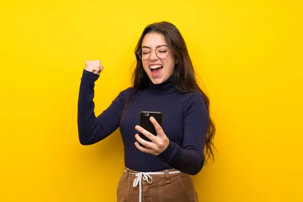 Tiener Meisje Geïsoleerde Gele Muur Met Telefoon Overwinnings Positie — Stockfoto