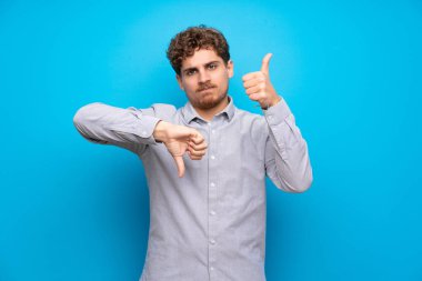 Mavi duvar iyi-kötü işaret yapma sarışın adam. Arasında kararsız Evet ya da değil