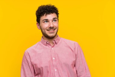 İzole sarı duvar üzerinde kıvırcık saçlı adam gülüyor ve yukarı bakıyor