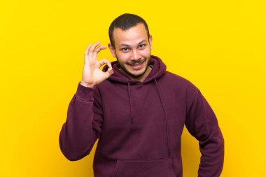 Parmakları ile ok işareti gösteren sarı duvar üzerinde sweatshirt ile Kolombiyalı adam
