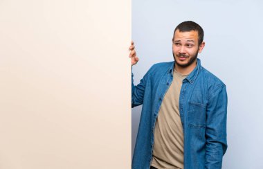 Kolombiyalı adam ayakta boş bir pankart tutarak ve yan bakıyor