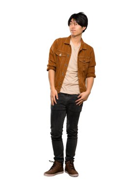 Kahverengi ceketli Asyalı bir adamın tam uzunlukta bir fotoğrafı, izole beyaz arka plan üzerinde yan bakarak şüpheler jest yapma