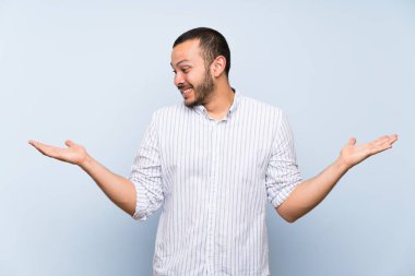 İki eliyle copyspace tutan izole mavi duvar üzerinde Kolombiyalı adam
