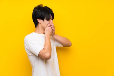 Ağız kapsayan izole sarı duvar üzerinde Asyalı adam ve yan bakıyor