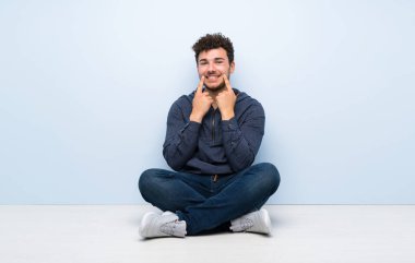 Genç adam yerde mutlu ve hoş bir ifadeyle gülümsüyor.