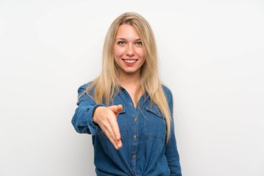 İzole edilmiş beyaz duvarın üzerinde genç sarışın kadın iyi bir anlaşma için el sıkışıyor.