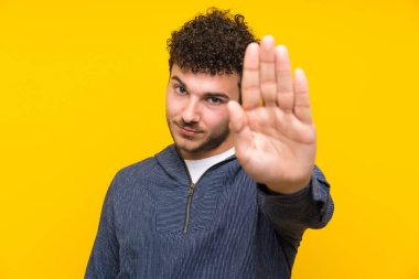 Sarı duvarın üstünde genç bir adam elleriyle jesti durduruyor.