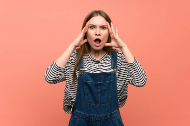 Sürpriz ve şok yüz ifadesi ile pembe duvar üzerinde tulum ile genç kadın