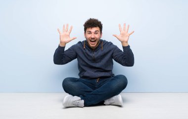 Genç adam yerde oturmuş parmaklarıyla 10 'a kadar sayıyor.